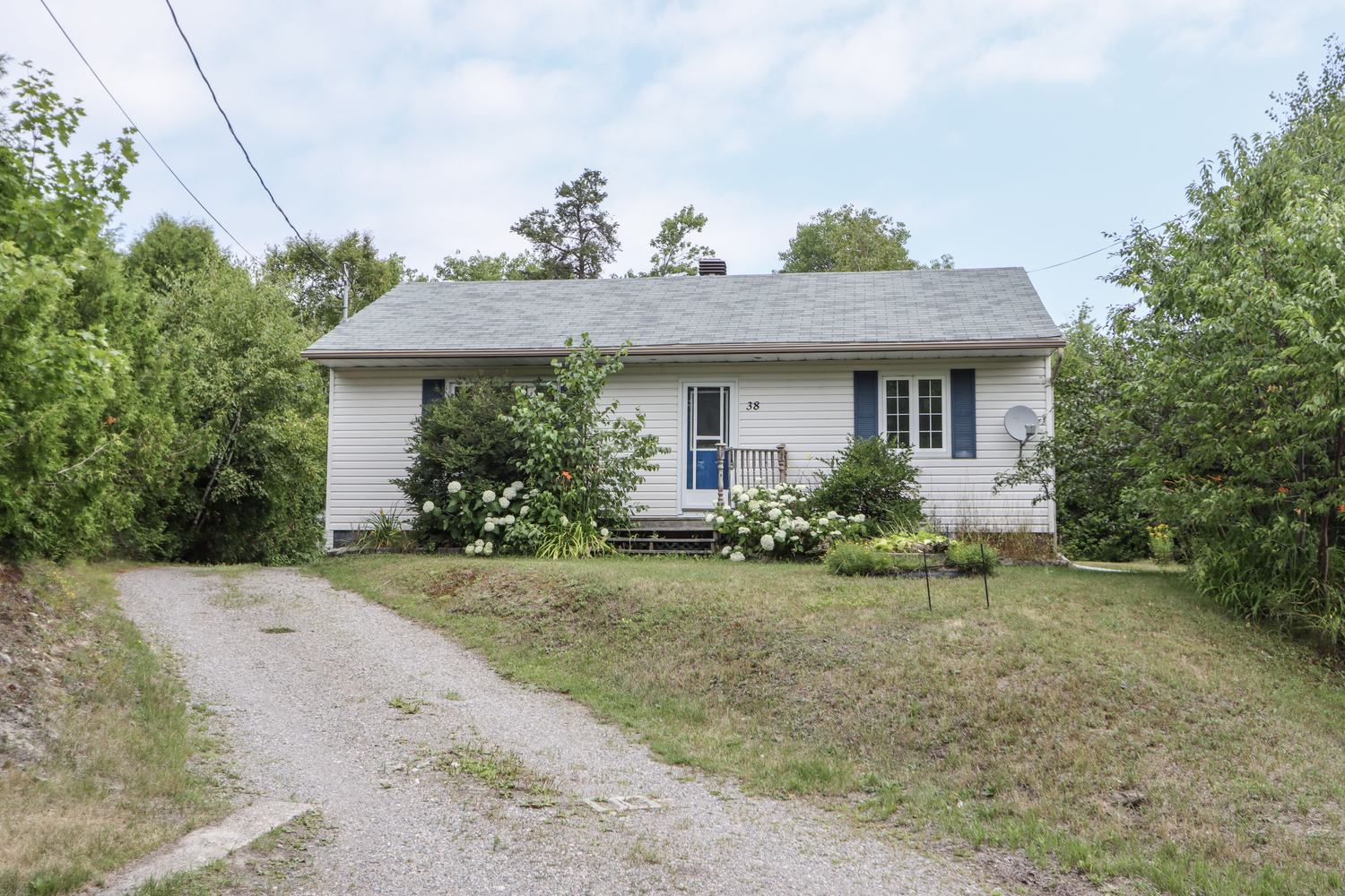 Front exterior of the white bungalow with a gravel driveway and green front lawn