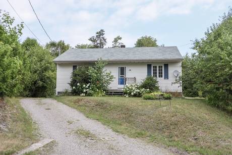 Front exterior of the white bungalow with a gravel driveway and green front lawn