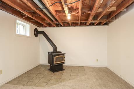 Black wood stove set on tile in an unfinished basement corner