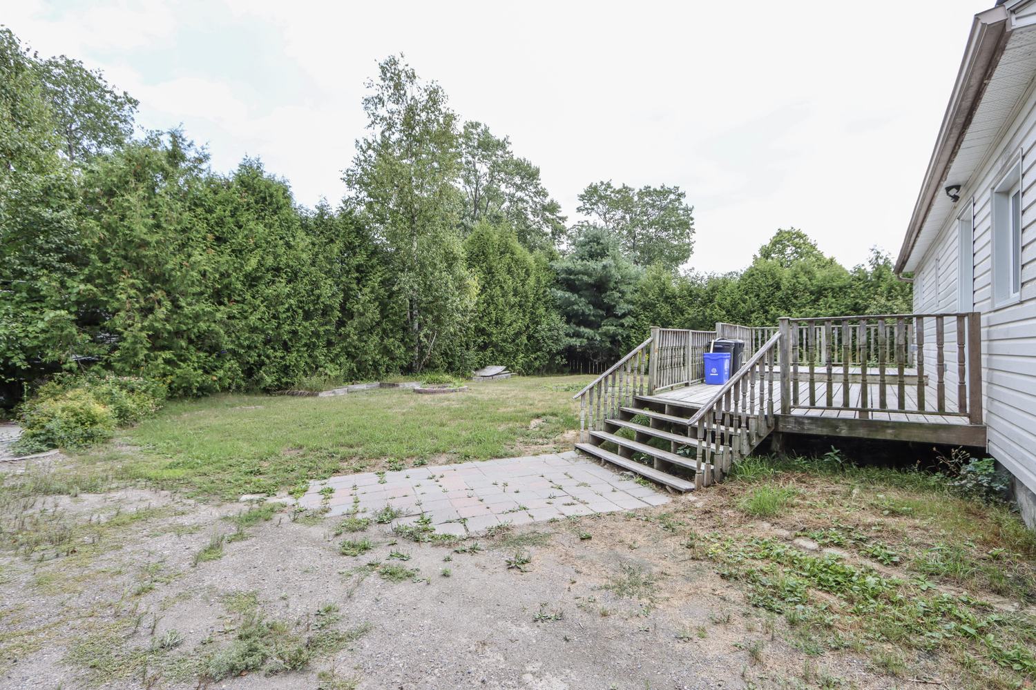 Rear wooden deck with stairs and a stone patio backed by trees