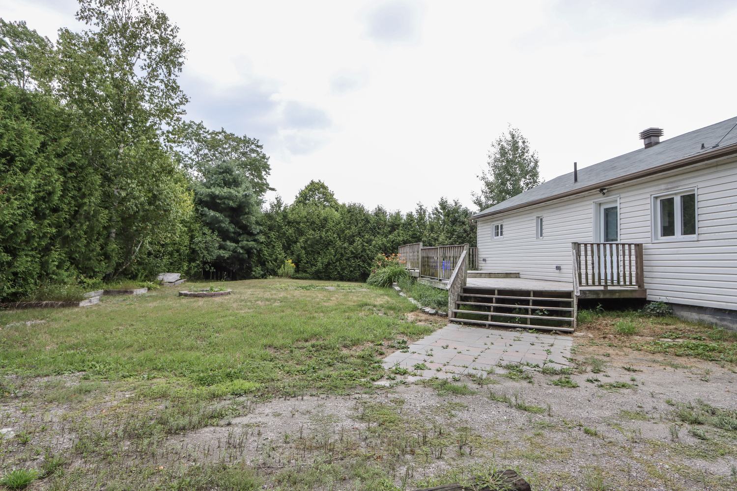 Back of the house with a wooden deck, lawn and mature trees