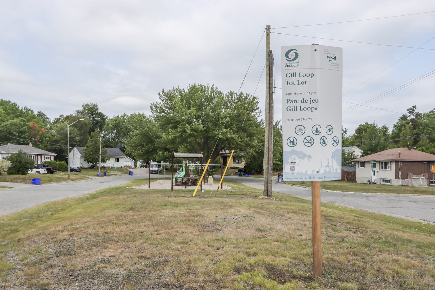 Neighbourhood park sign and playground equipment across a residential street